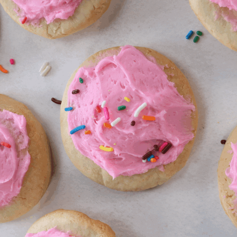 Soft frosted copycat Crumbl sugar cookies topped with pink almond frosting on a white plate.