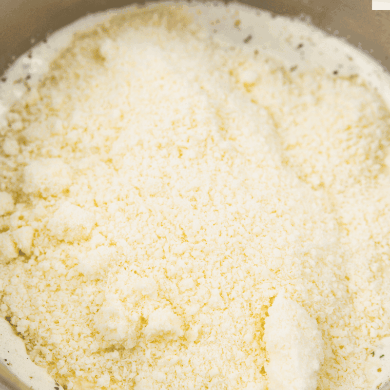Grated Parmesan and shredded mozzarella cheese melting into creamy sauce.