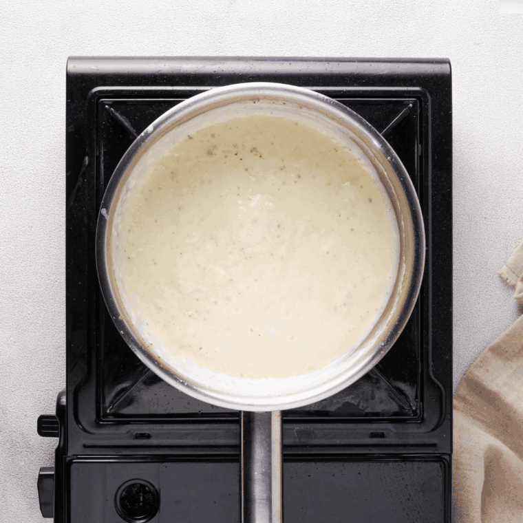 Seasoning the Alfredo sauce with salt, black pepper, and optional herbs.