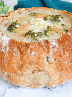 Creamy Copycat Subway Broccoli and Cheese Soup in a white bowl topped with shredded cheddar and fresh broccoli florets.