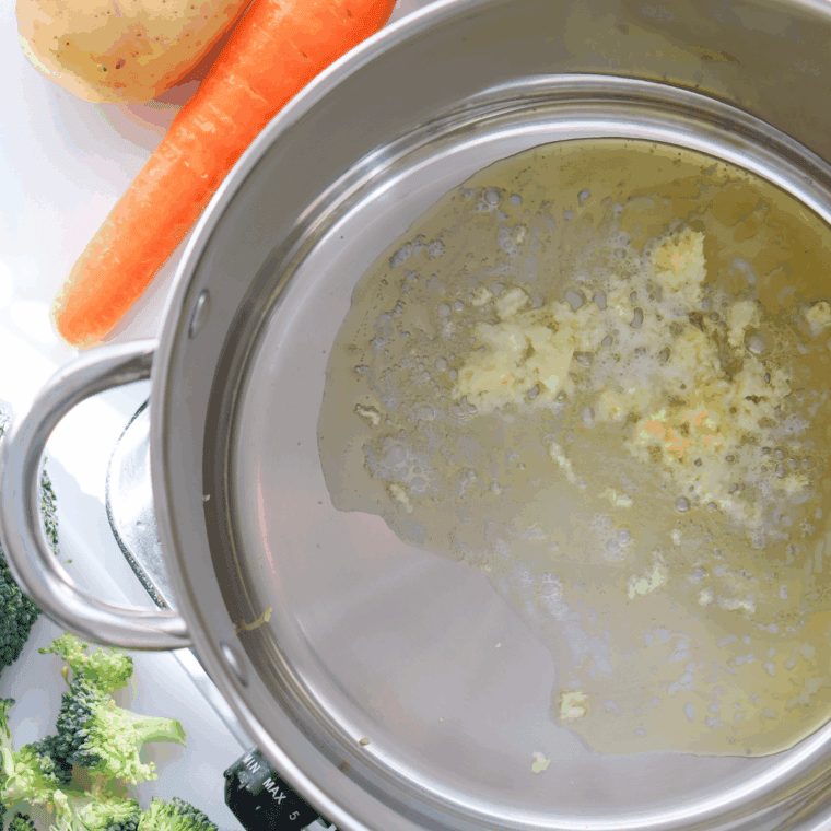 Onion and garlic sautéing in melted butter in a large pot, creating a fragrant base for broccoli cheddar soup.