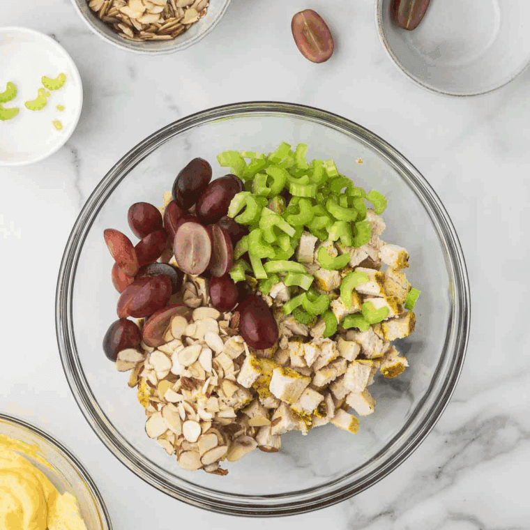 Mixing chicken, apple, grapes, celery, raisins, and almonds with curry dressing.