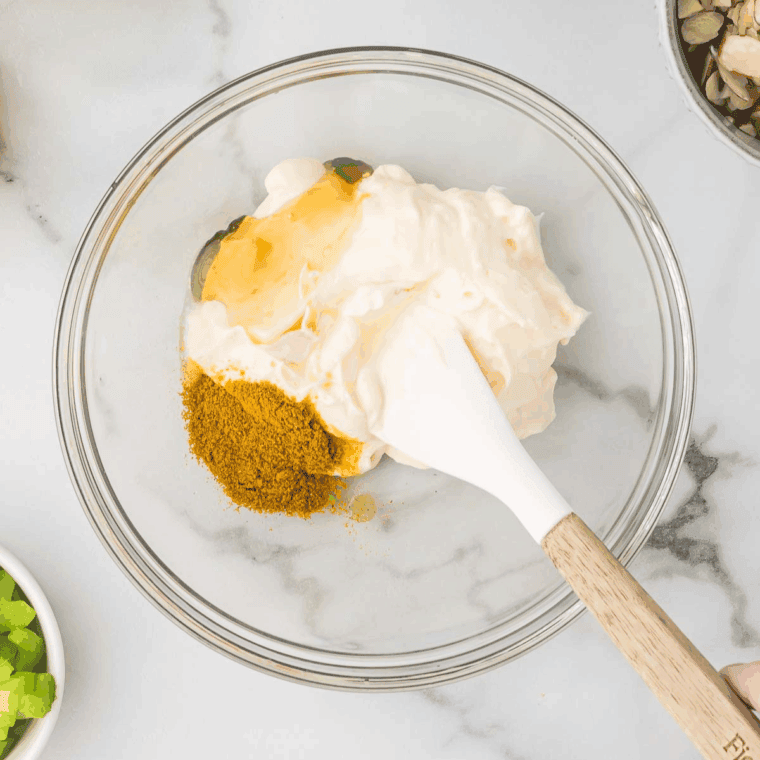 Whisking mayonnaise, Greek yogurt, curry powder, and lemon juice in a bowl.