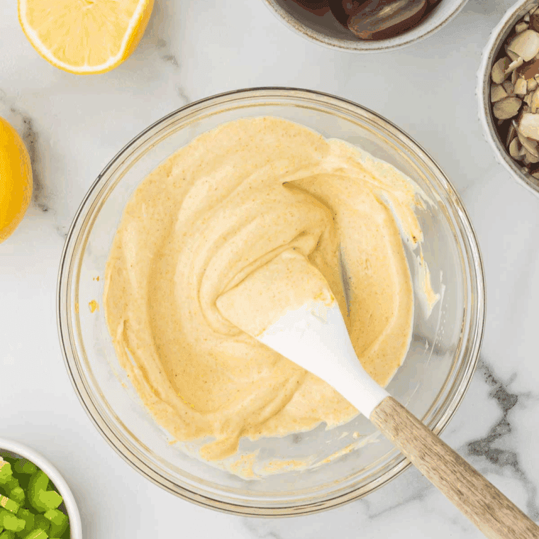 Mixing chicken, apple, grapes, celery, raisins, and almonds with curry dressing.
