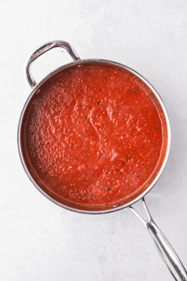Freshly made Ina Garten marinara sauce simmering in a pan with tomatoes and herbs.