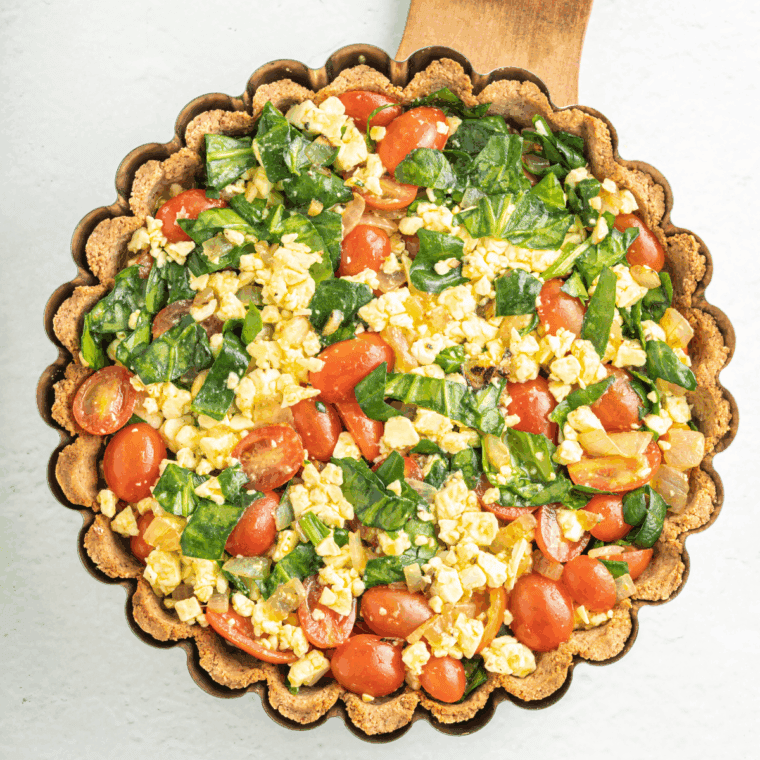 Pouring quiche filling into a partially baked pie crust evenly.