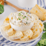 A bowl of creamy Lipton Onion Soup Spinach Sauce with crackers and fresh vegetables on a wooden board ready as a party snack.