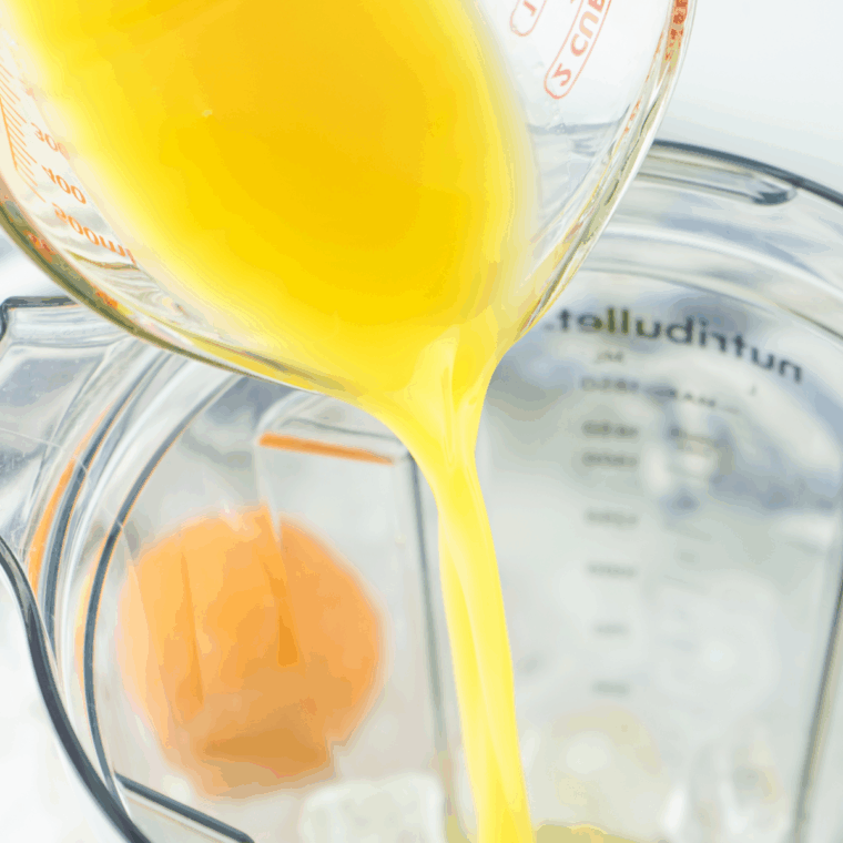 Pouring orange juice and sparkling wine into a large measuring cup to prepare a frozen mimosa.