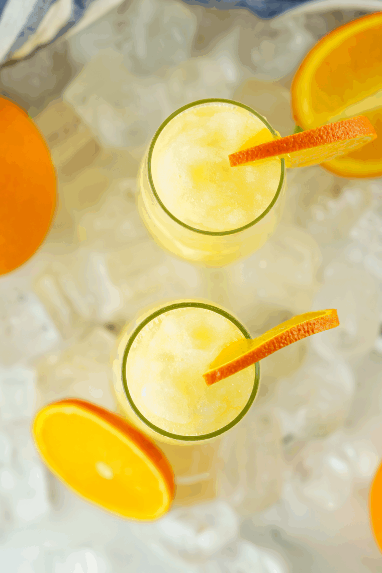 Glass of frozen mimosa made with orange juice and sparkling wine, garnished with an orange slice.