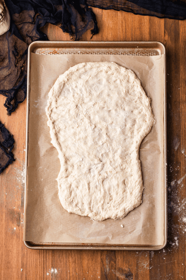 Rolling out pizza dough and cutting it into a skull shape on the baking sheet.