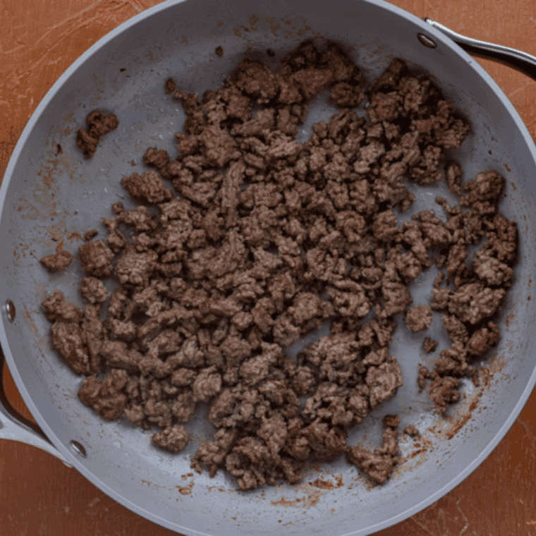 Ground beef and chopped onions cooking in a skillet until browned for cheeseburger pie.