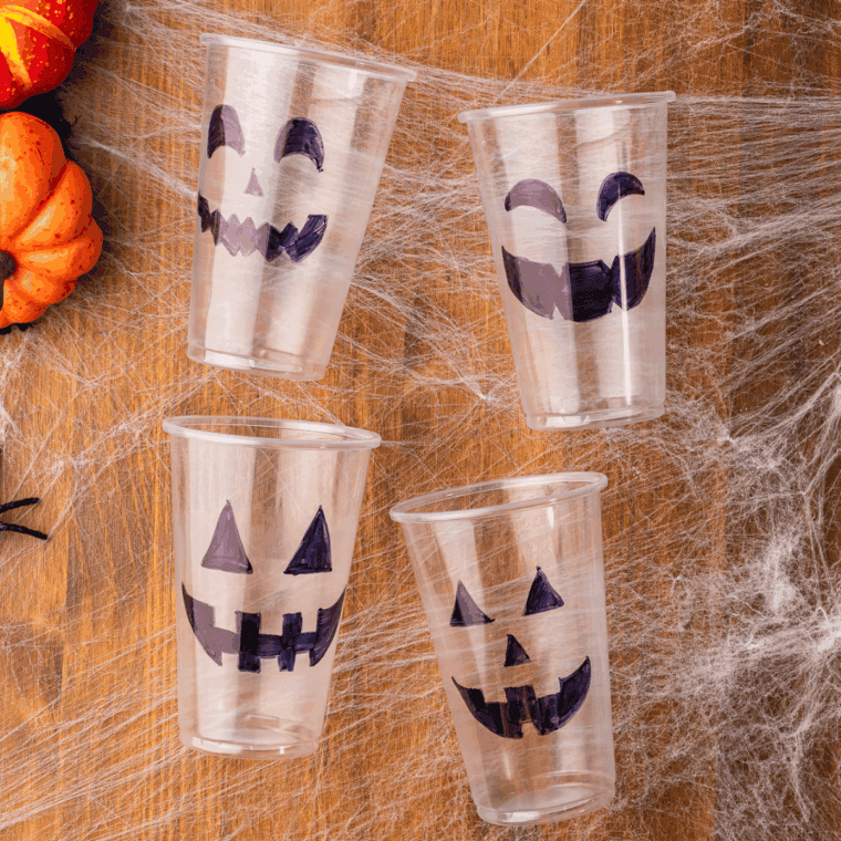 Drawing Jack-O’-Lantern faces on clear plastic cups using a black Sharpie.