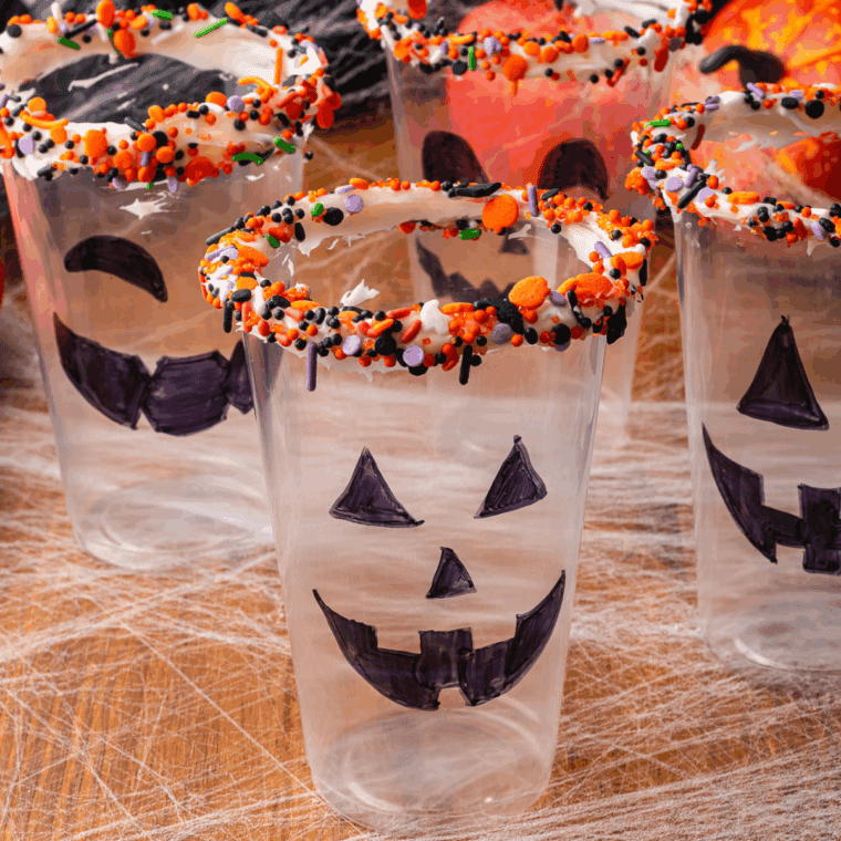 Dipping the rim of a plastic cup in frosting and Halloween sprinkles.