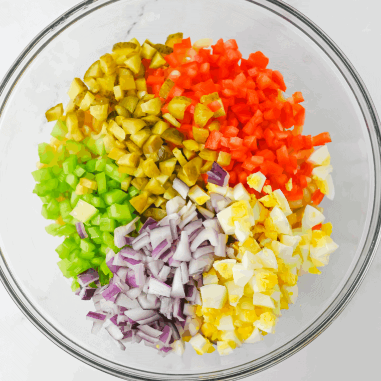Finely chopped celery, red bell pepper, and red onion mixed into dressing, then gently folded with cooled pasta.
