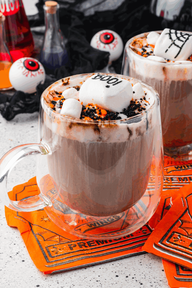 Cup of hot cocoa topped with Halloween-themed whipped cream and sprinkles.
