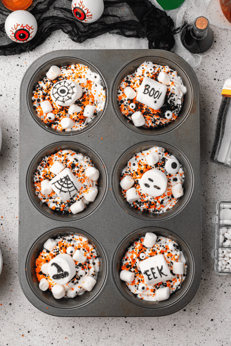 Cup of hot cocoa topped with Halloween-themed whipped cream, marshmallows, and sprinkles.