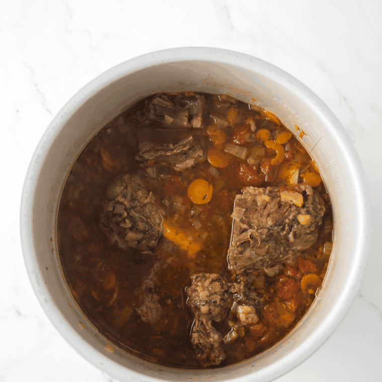 White wine being poured into the pan to deglaze browned bits, with herbs and chicken stock ready to add.