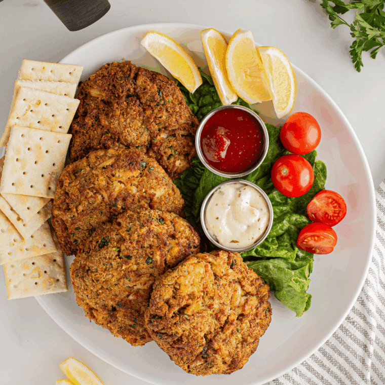 Cooked golden crab cakes served on a plate with lemon wedges and a side of remoulade sauce.