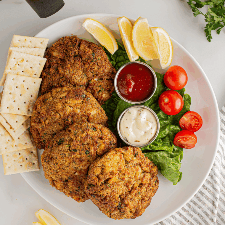 Golden-brown crab cakes pan-fried to perfection, served with lemon wedges and fresh herbs.