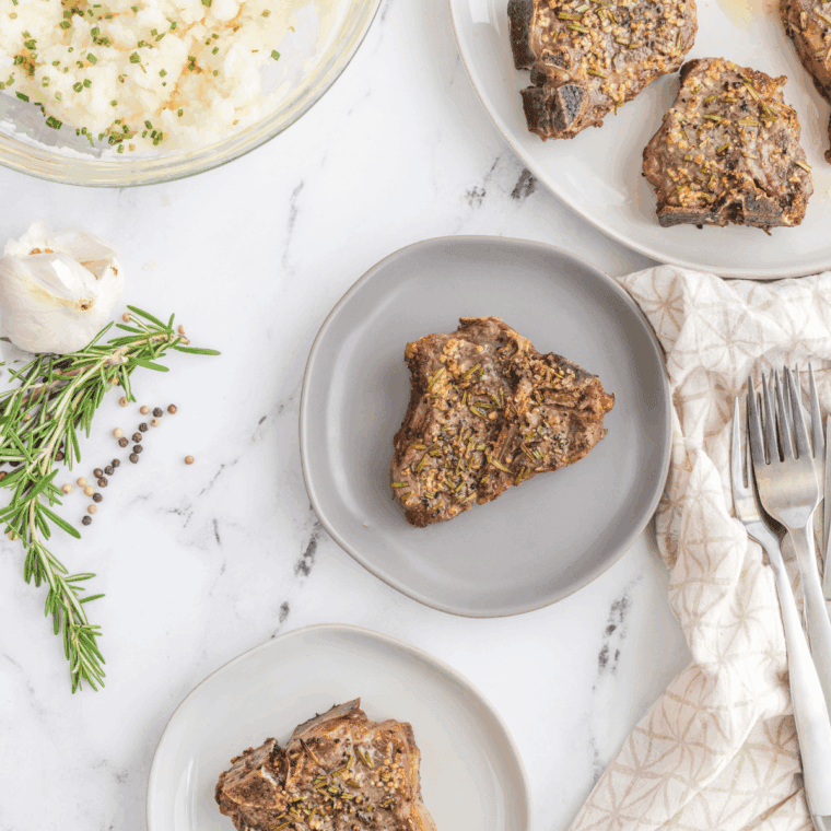 Rested Moroccan grilled lamb chops on a plate, garnished with lemon juice and fresh herbs.