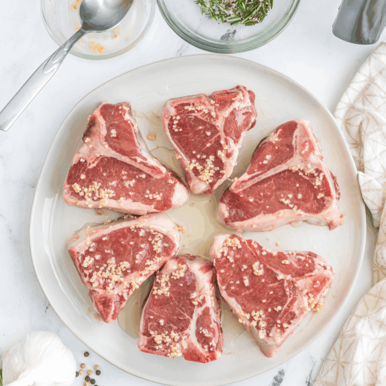 Lamb chops being coated with Moroccan spice marinade before resting for flavor.