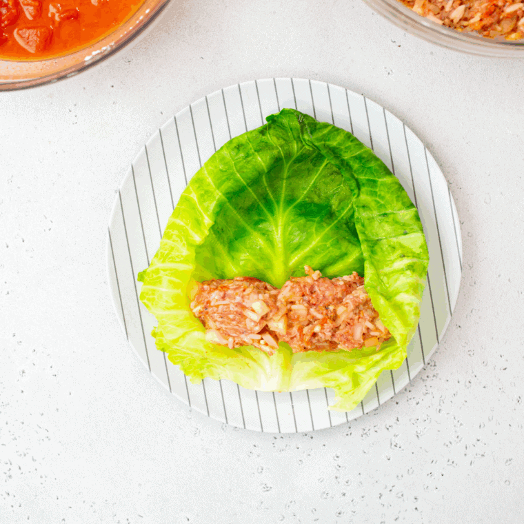 Assembling stuffed cabbage rolls by filling cabbage leaves with raw meat mixture and rolling tightly.