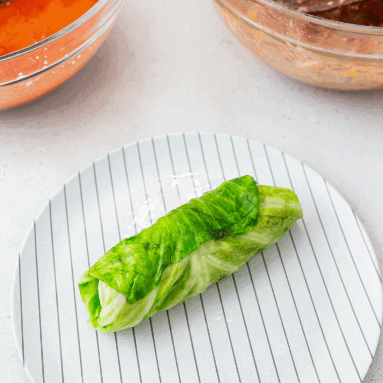 Rolling cabbage leaves around seasoned raw beef and rice mixture to form individual rolls.