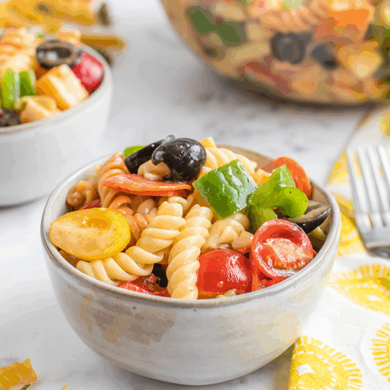 Close-up of creamy Jason’s Deli-style pasta salad with diced bell peppers, shredded cheese, and fresh greens in a bowl.