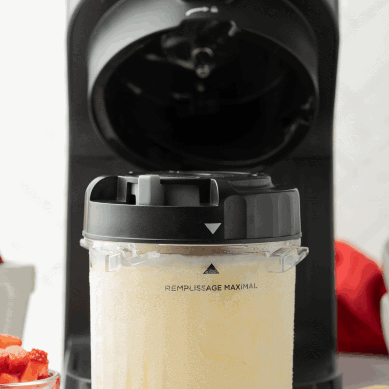 Frozen pint inserted into Ninja Creami machine, ice cream being processed to creamy consistency.