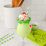 Tall glass of green Grinch milkshake topped with whipped cream and holiday sprinkles, ready to serve.