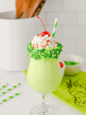 Tall glass of green Grinch milkshake topped with whipped cream and holiday sprinkles, ready to serve.