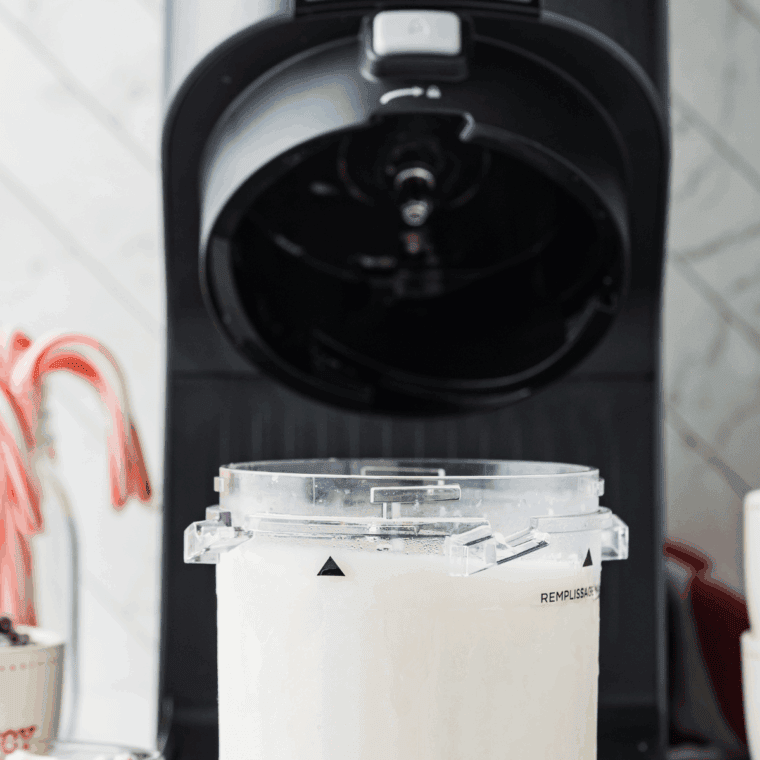 Pint container locked in Ninja Creami machine, churning milkshake to creamy consistency.