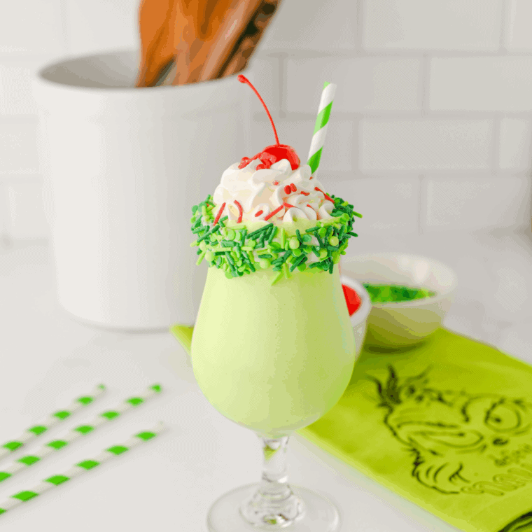 Tall glass of green Grinch milkshake topped with whipped cream and holiday sprinkles, ready to serve.