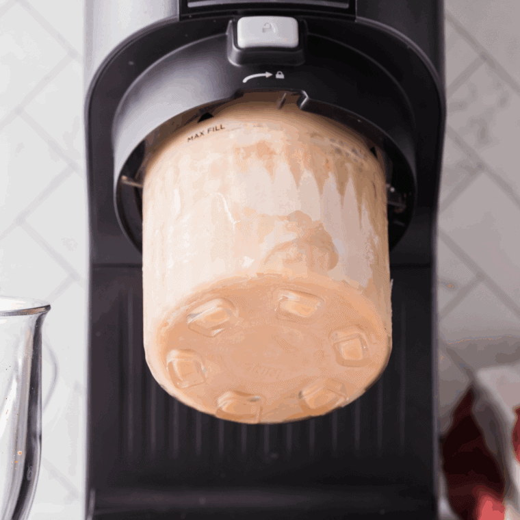 Frozen Ninja Creami pint placed into the machine, blending on the “Creamiccino” setting to create a smooth peppermint mocha drink.