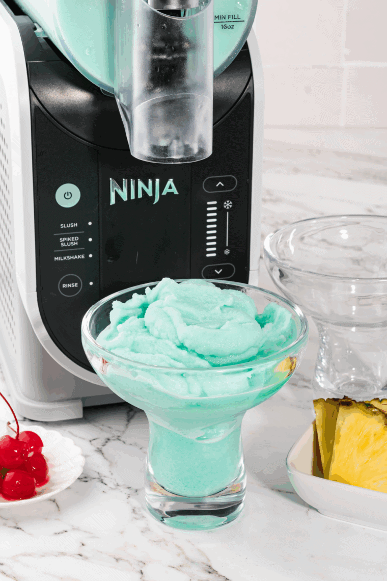 Glass of frozen Blue Hawaiian cocktail made with Ninja Slushi, garnished with pineapple wedge and cherry