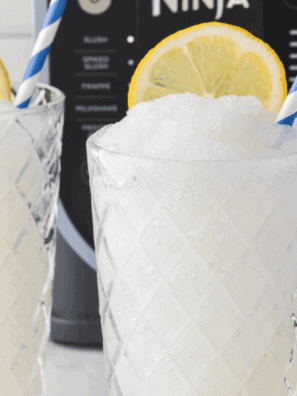 Frosted lemonade slushie made in a Ninja blender, served in a glass with lemon slices and a straw.