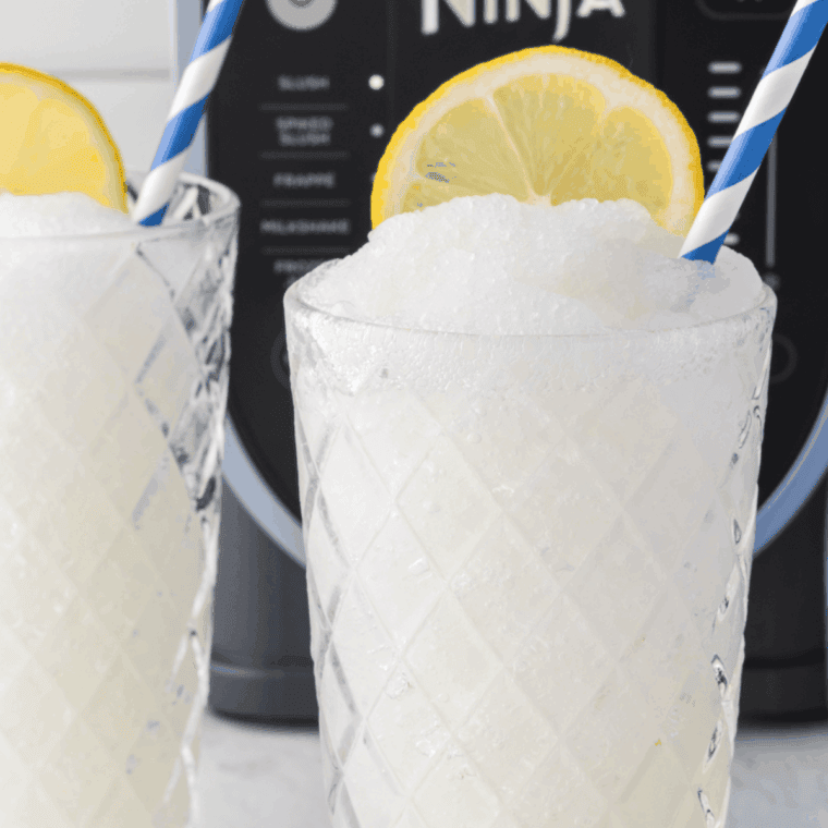 Frosted lemonade slushie made in a Ninja blender, served in a glass with lemon slices and a straw.