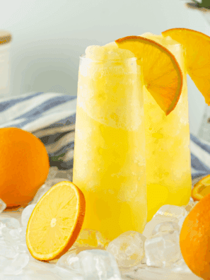 Glass of frozen mimosa slush made with orange juice and champagne, topped with an orange slice and served with a straw.
