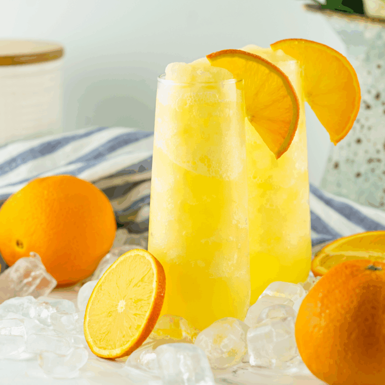 Glass of frozen mimosa slush made with orange juice and champagne, topped with an orange slice and served with a straw.