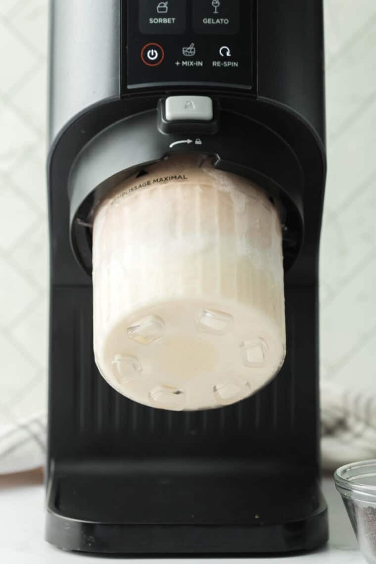Frozen pint container being processed in a Ninja Creami using the ice cream function until creamy.