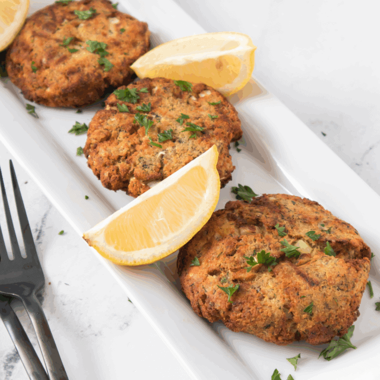 Golden-brown Pioneer Woman salmon patties served on a plate with lemon wedges and fresh herbs.