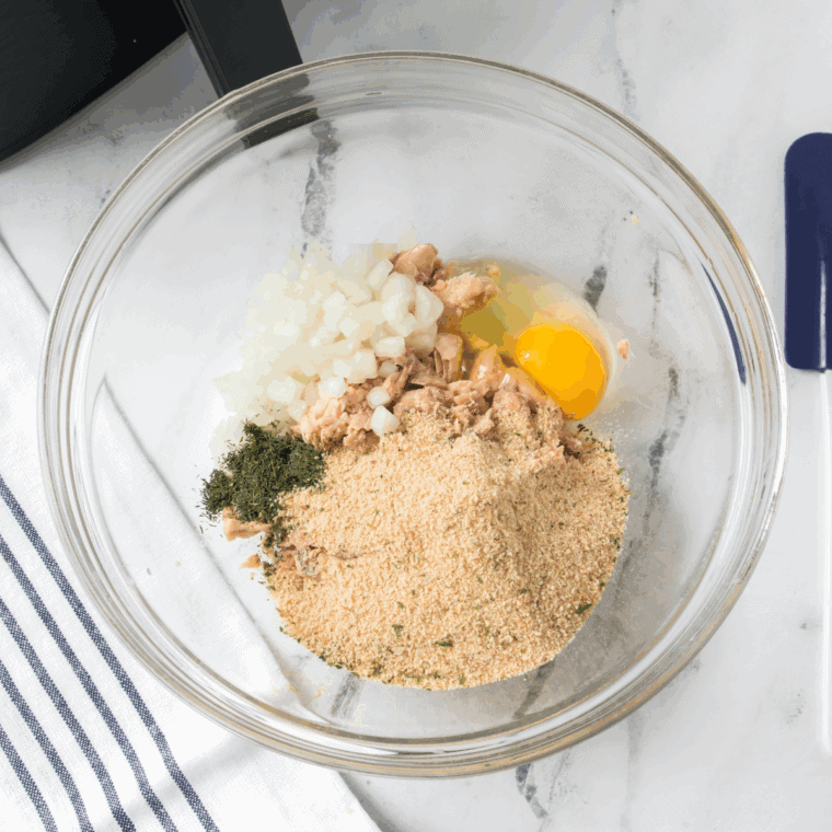 Mixing flaked canned salmon, eggs, breadcrumbs, mayonnaise, mustard, green onions, lemon juice, and seasonings in a large bowl.