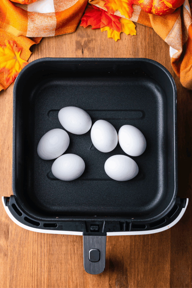 Eggs cooking in an air fryer basket in a single layer for hard-boiled deviled eggs.