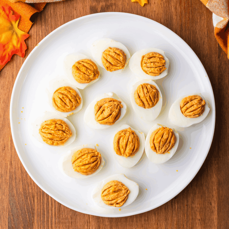 Deviled eggs decorated with lines to resemble pumpkins and topped with chives as stems.
