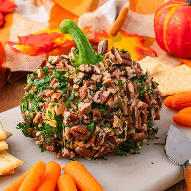 Pumpkin-shaped cheese ball served on a platter with crackers and herbs for a festive Halloween or Thanksgiving appetizer.
