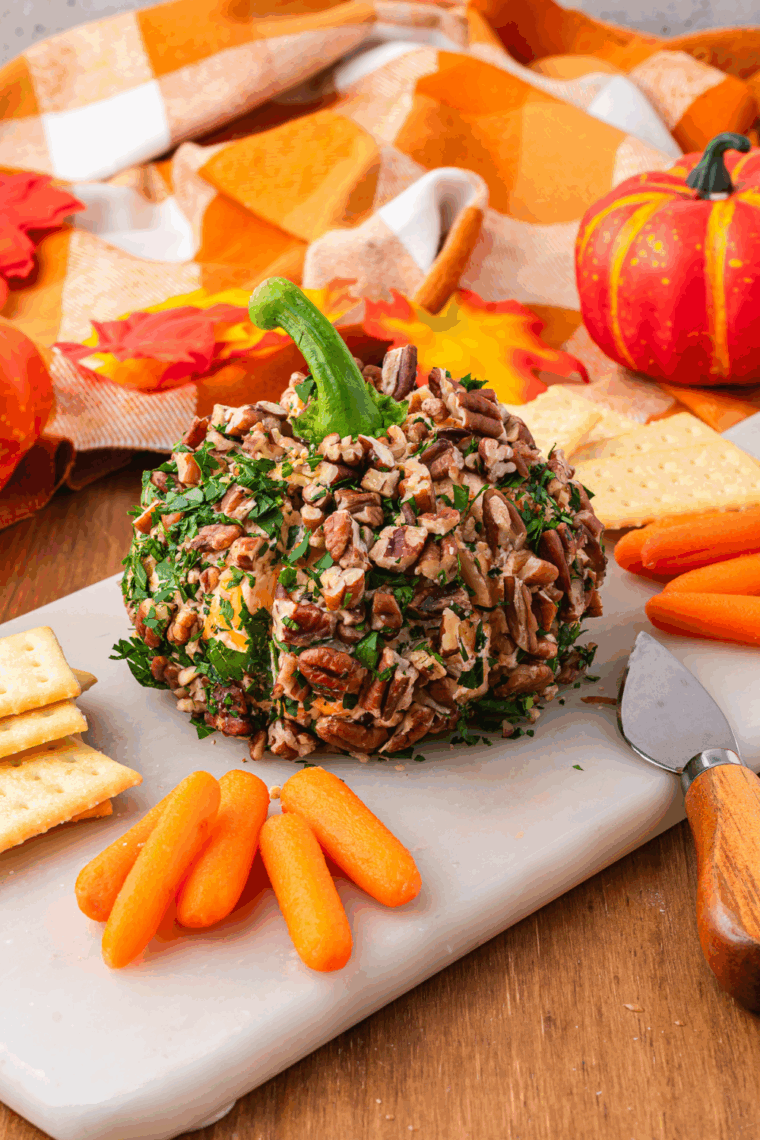 Pumpkin-shaped cheese ball on a serving platter surrounded by crackers, bread, and vegetables, ready for Halloween or Thanksgiving.