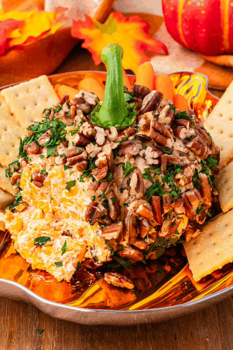 Pumpkin shaped cheese ball served on a platter with crackers and pretzels for a festive Halloween or Thanksgiving appetizer.