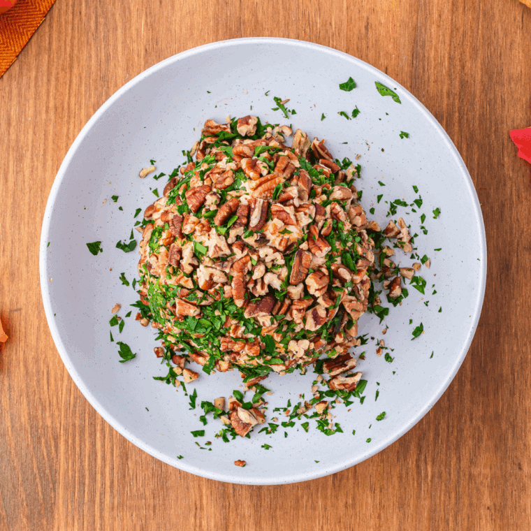 Coating the chilled cheese ball with chopped nuts and herbs, adding a green bell pepper or chive “stem,” and arranging on a platter with crackers, bread, and vegetables