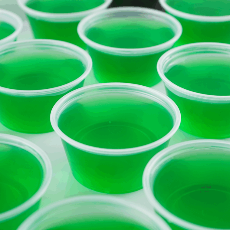 Arranging green and brown Jello shot cups in a Christmas tree shape on a flat surface.