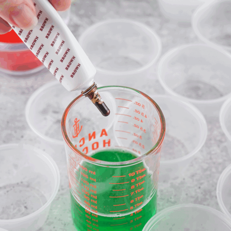 Pouring green and brown Jello mixtures into individual plastic shot cups for setting.